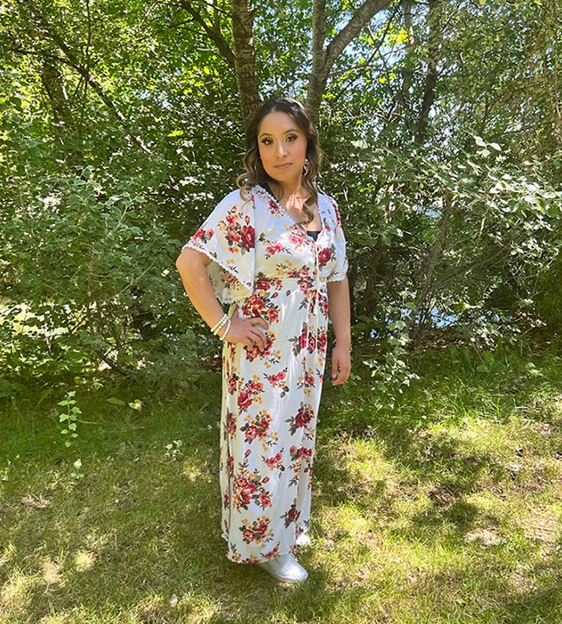 Angelica Gomez stands in front of bushes and trees.